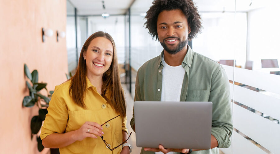 Woman in yellow shirt holding glasses standing next to man in green shirt holding MacBook laptop