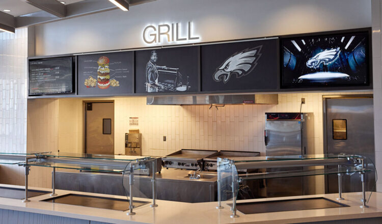 a kitchen and grill station with BrightSign digital signage playing on screens above industrial fan