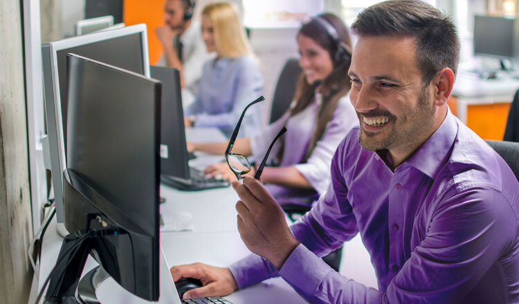 Smiling BrightSign customer support agent taking off glasses and working on computer