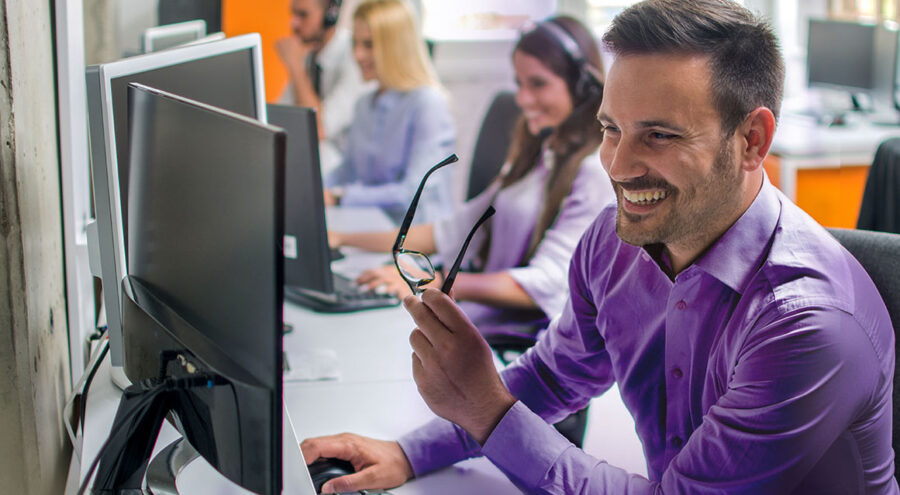 Smiling BrightSign customer support agent taking off glasses and working on computer
